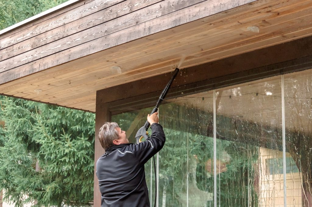 Man cleaning walls and floor with high pressure power washer. Washing terrace wood planks and claddi